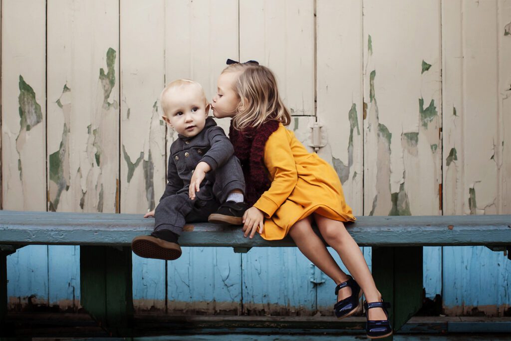 Little-Girl-in-Yellow-Dress-Kissing-Baby-Brother-on-a-Bench